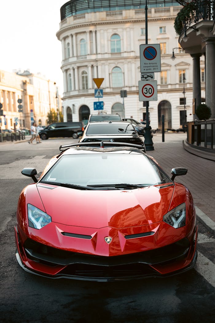 Front view of a sleek red sports car parked on a city street, showcasing urban architecture.